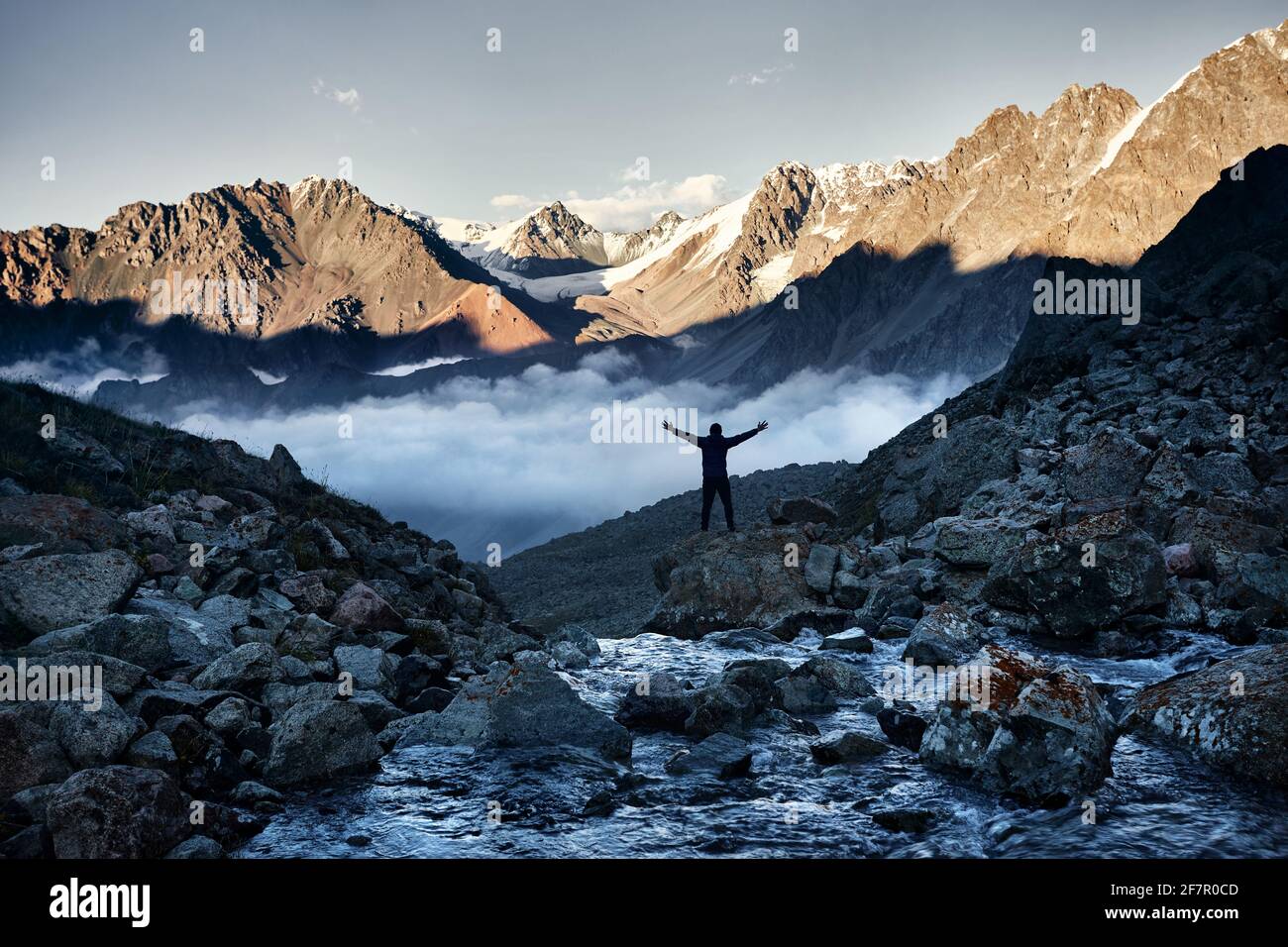 Hiker in silhouette with hands up above the clouds against mountains with snow in Kazakhstan. Outdoor and hiking concept Stock Photo