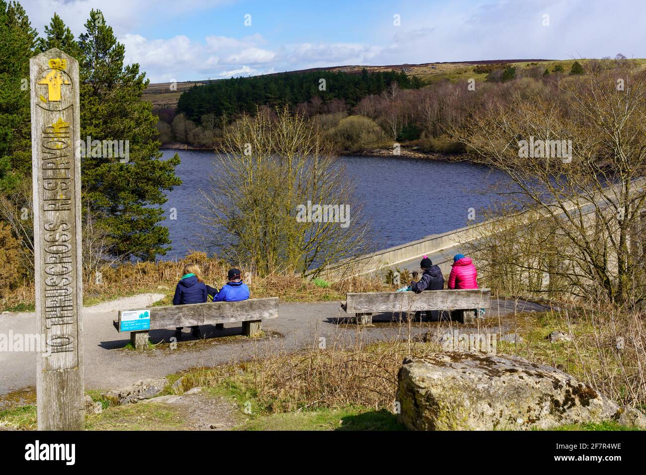 Wooden public path sign indicating Thruscross Reservoir with tourists sitting on benches enjoying the view, Washburn Valley, Harrogate, UK. Stock Photo