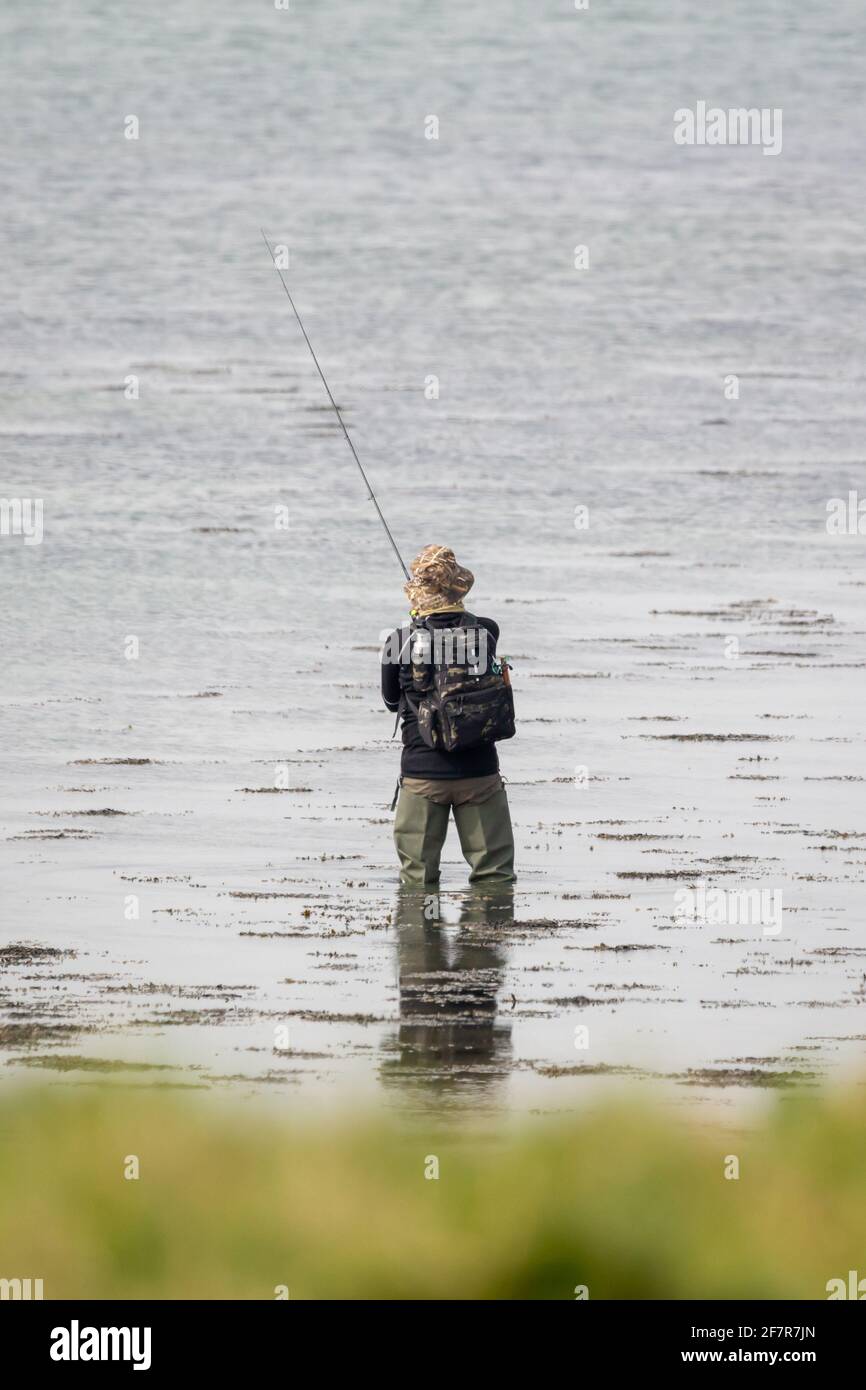 A fisherman fishing wearing waders and holding a fishing rod Stock Photo