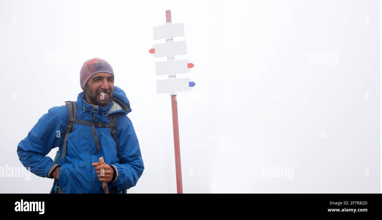 Happy adult man climbing stand near blank arrows in fog mountain. Copy space. Stock Photo