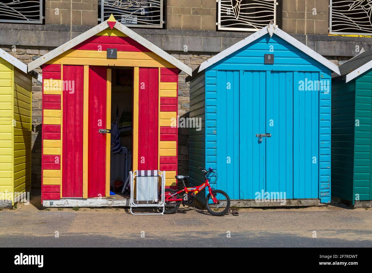 Childs red bike and foldable chair outside colourful beach huts at Boscombe, Bournemouth, Dorset UK in April Stock Photo