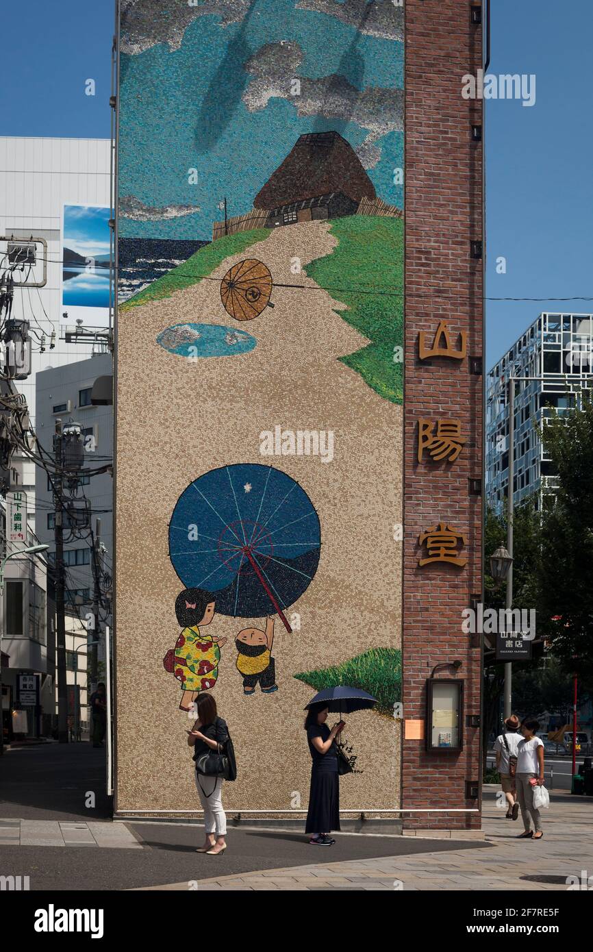 Vertical view of two young women using their mobile phones in front of a giant Japanese mosaic at Omote-Sando with Aoyama-Dori Ave crossing, Harajuku Stock Photo