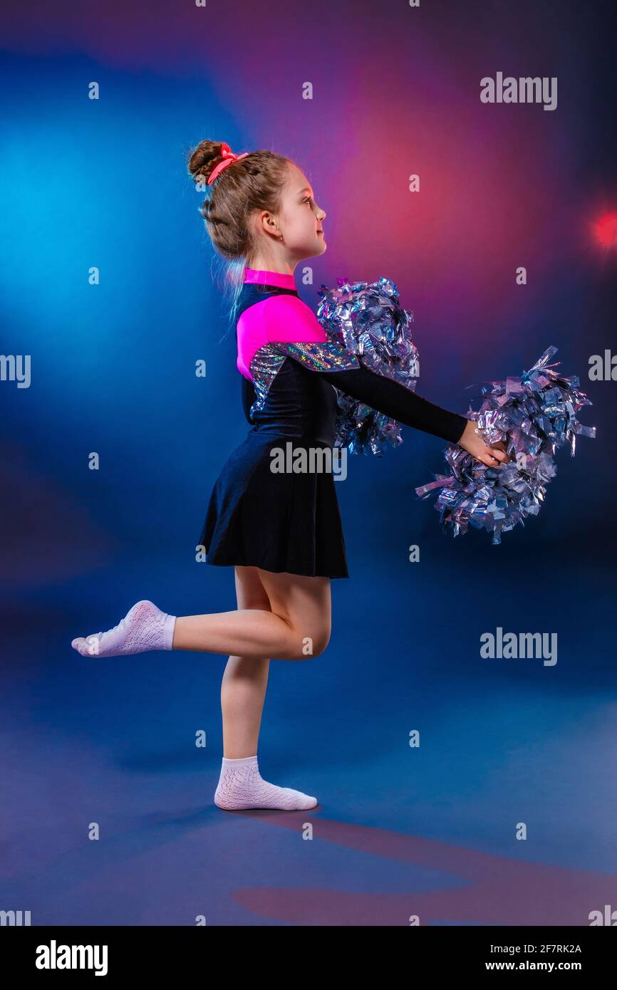 Little cheerleader practicing dance elements in studio with color light Stock Photo