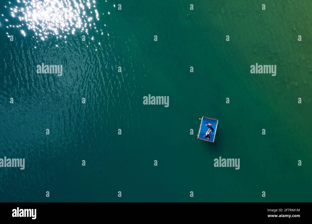 Suntanning couple on floating platform aerial top view. Bright sn reflecting in green lake waves. Peruca Lake, Dalmatia, Croatia Stock Photo