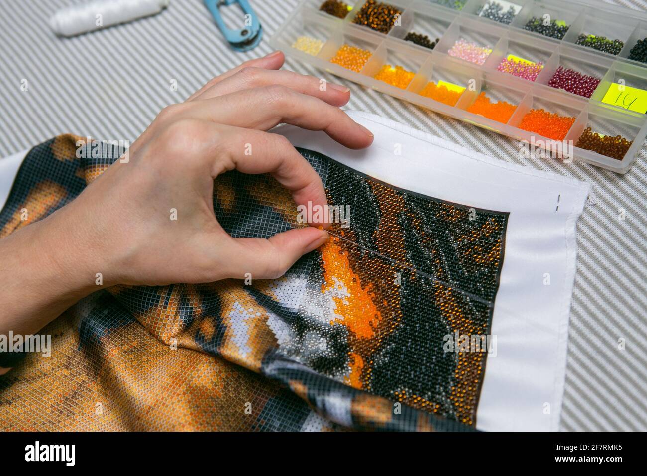 Bead embroidery process. Close-up - female hands string beads on a needle and sew them to the fabric. The woman is fond of embroidery. Stock Photo