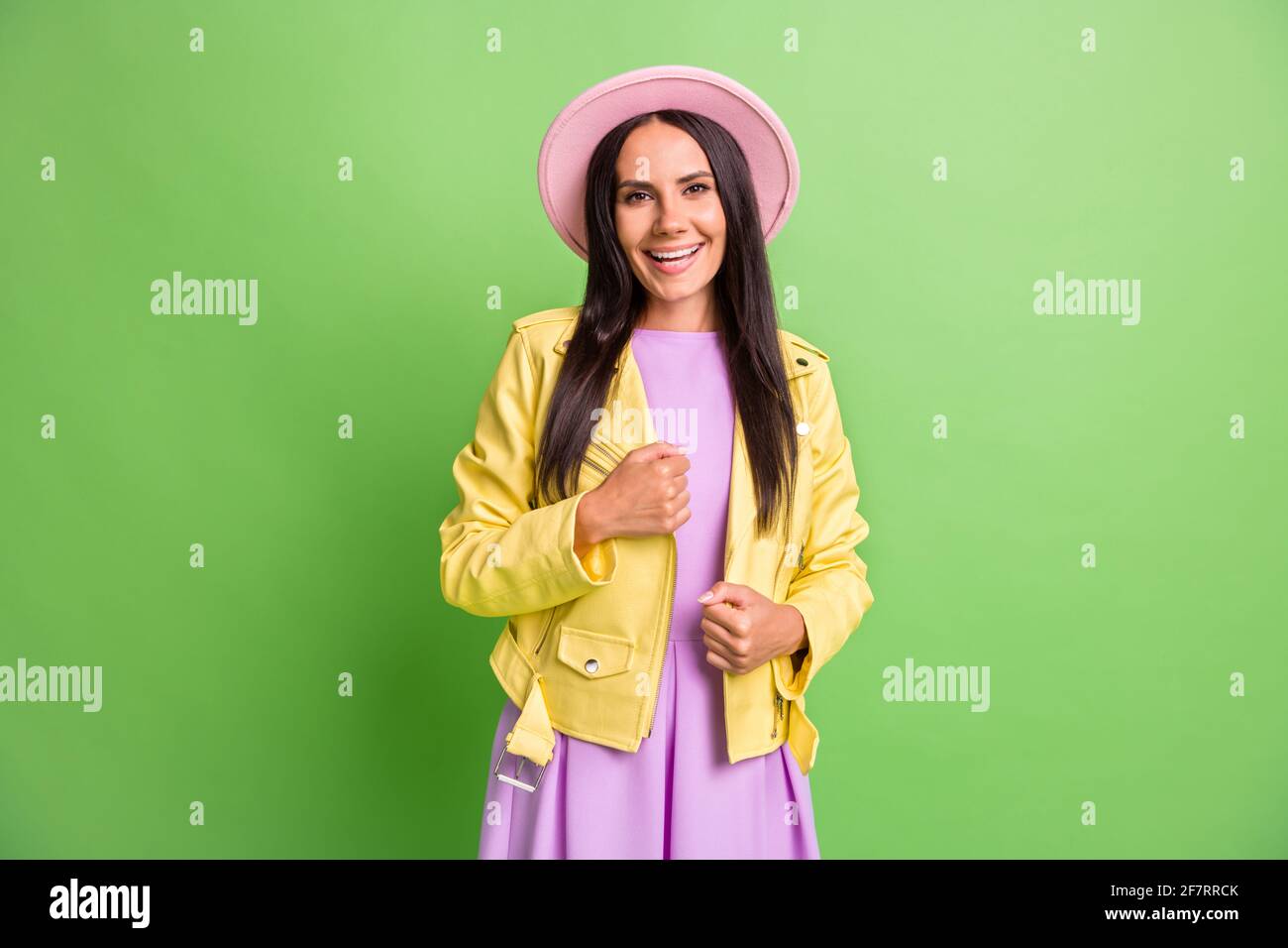 Photo portrait of brunette girl in pink hat yellow leather jacket smiling isolated on bright green color background Stock Photo