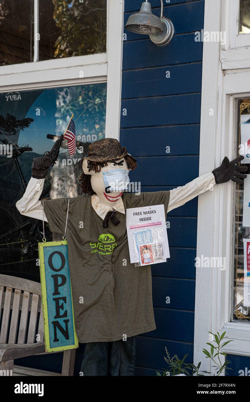 Masked mannequin in Downieville in front of an open store, with a gun pointing up with an American flag. The sign says “free masks inside”. Downievill Stock Photo