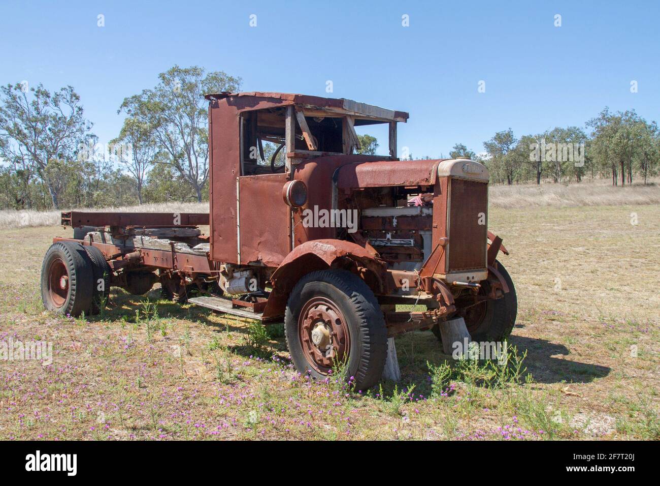 Old and rusting Leyland truck / lorry abandoned in grassy field under blue sky near ruins of historic steam sawmill in Australia Stock Photo