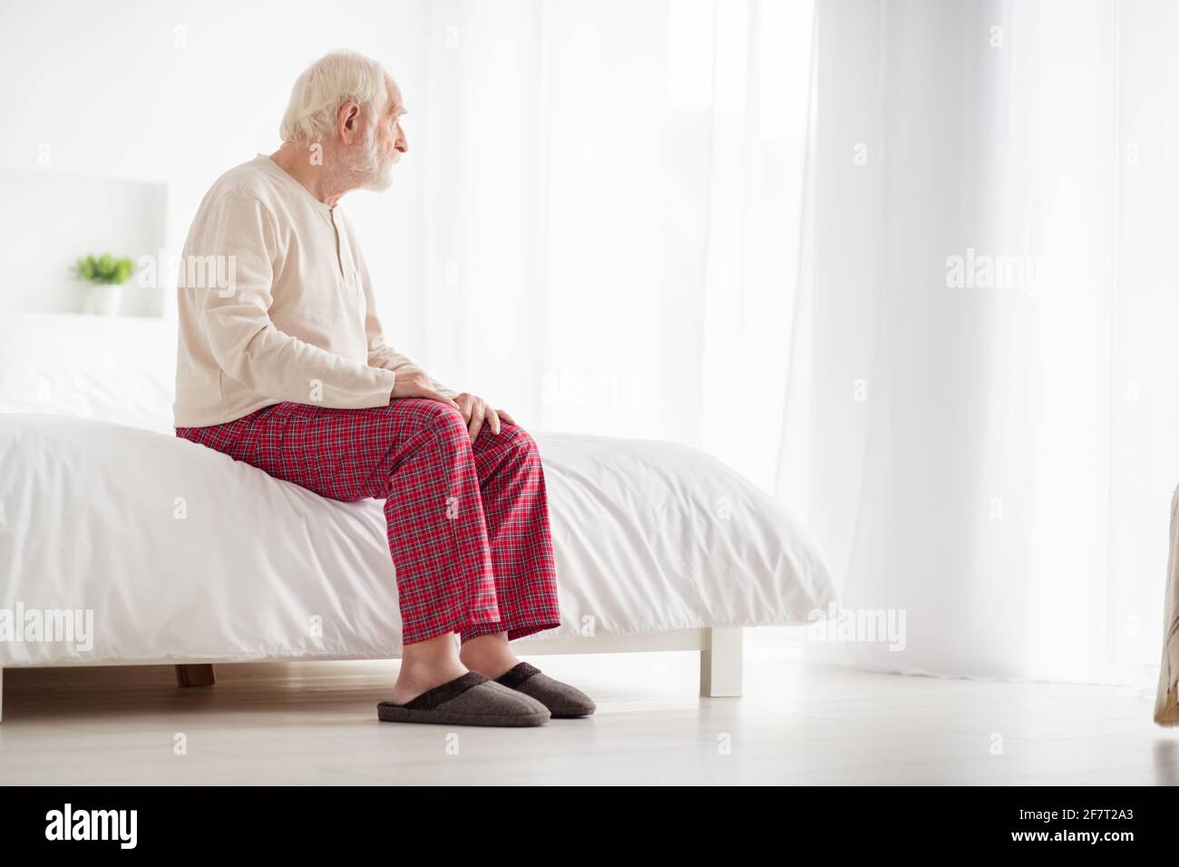 Photo of lonely frustrated age pensioner sleepwear sitting bed looking window inside indoors home room Stock Photo