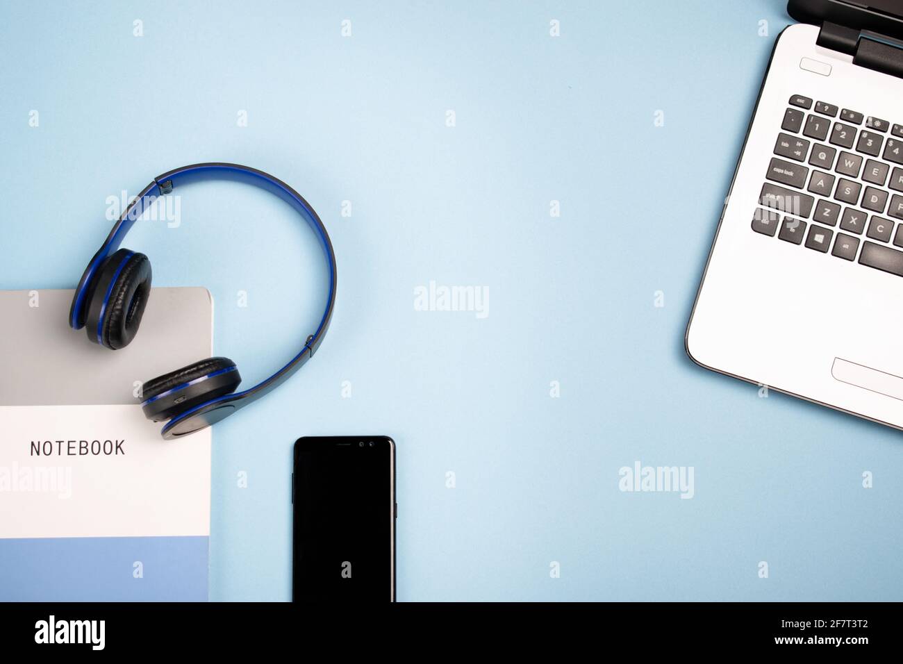 Notebook, headphones a mobile phone and laptop on a blue surface with a copy space Stock Photo