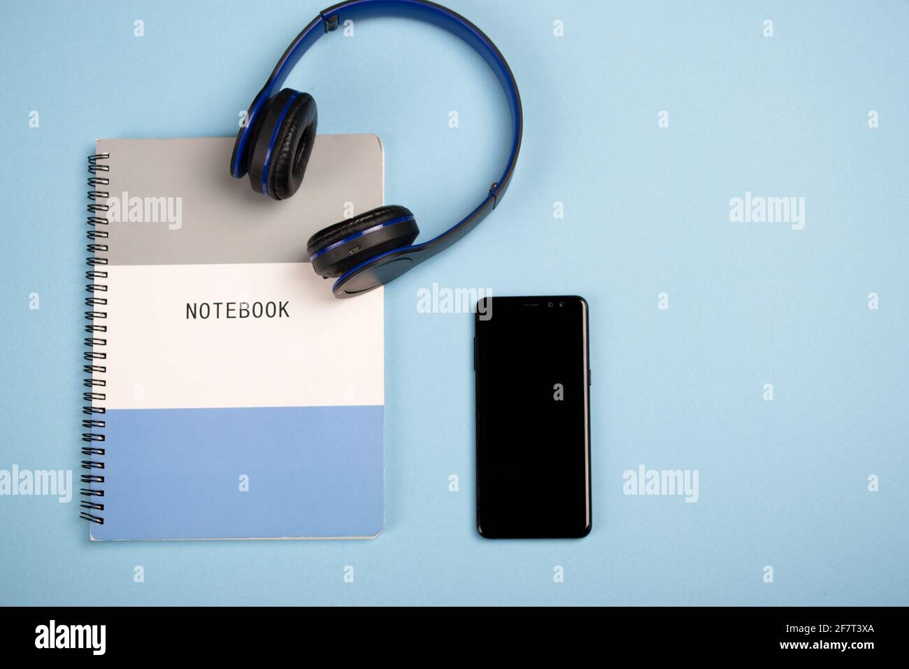 Notebook, a mobile phone and headphones on a blue surface - copy space Stock Photo