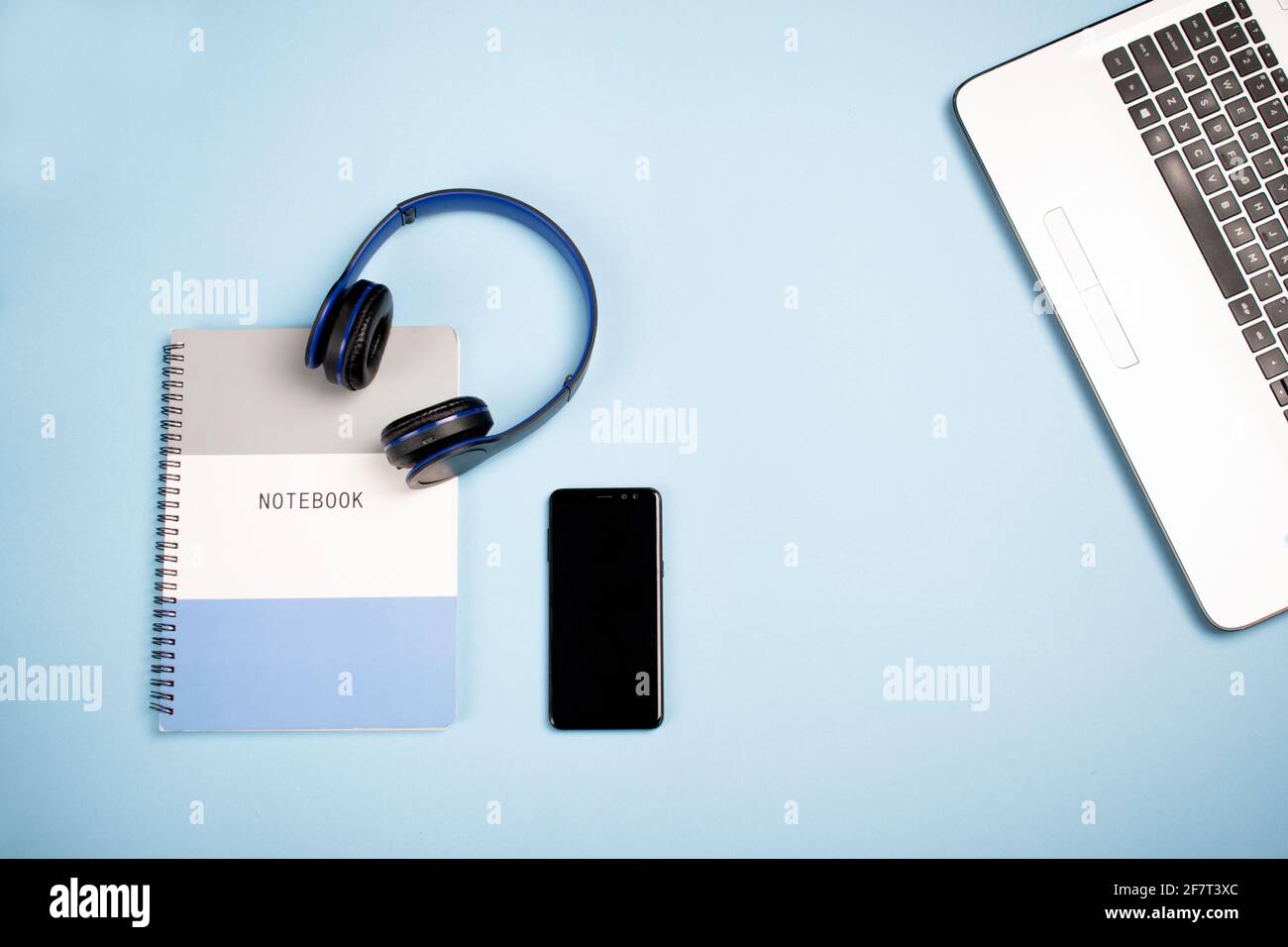 Notebook, headphones a mobile phone and laptop on a blue surface with a copy space Stock Photo