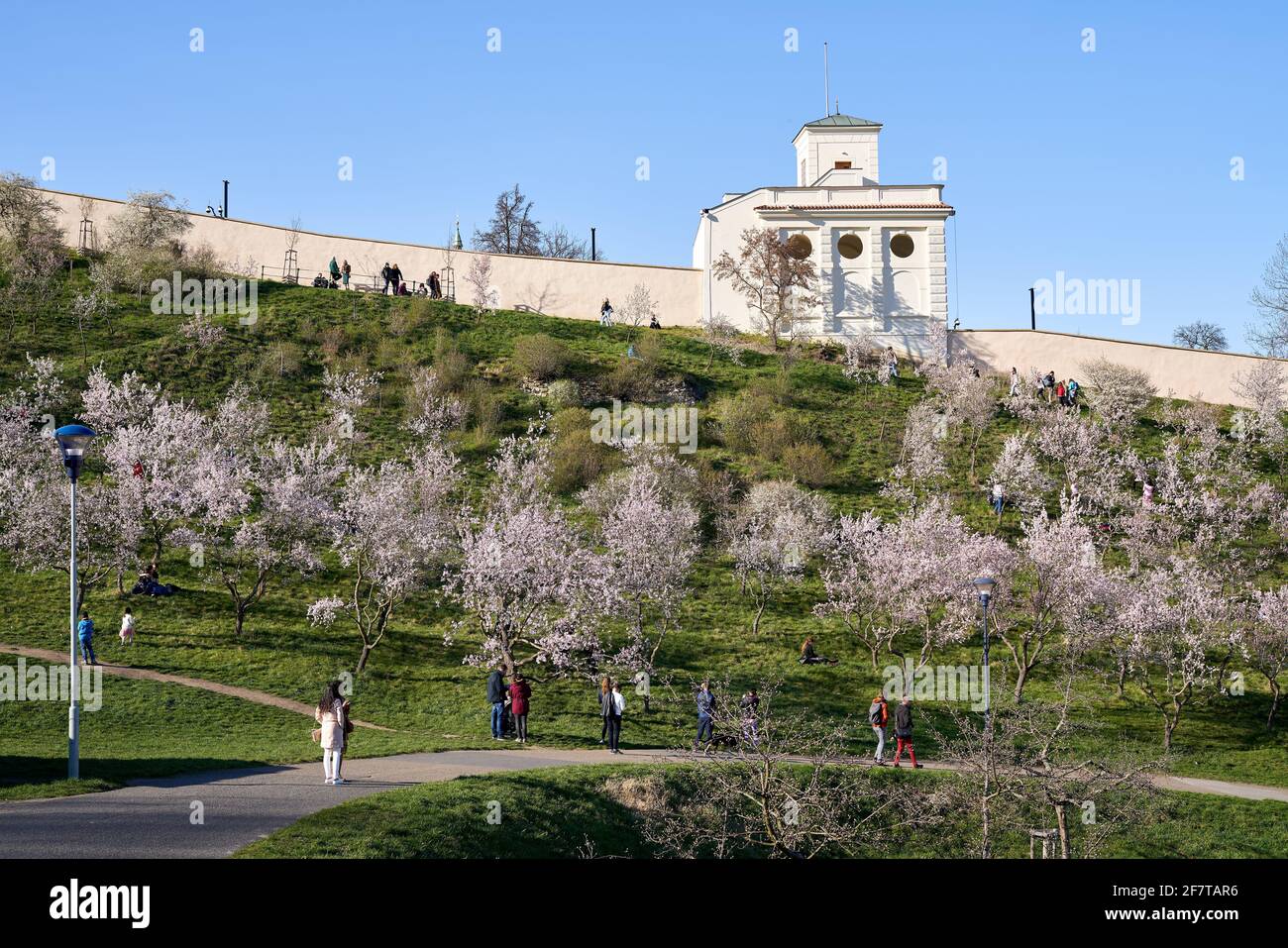 PRAGUE, CZECH REPUBLIC - APRIL 4, 2020: Schonbornska garden with blooming trees, people walking around and the U.S. Embassy in the background Stock Photo