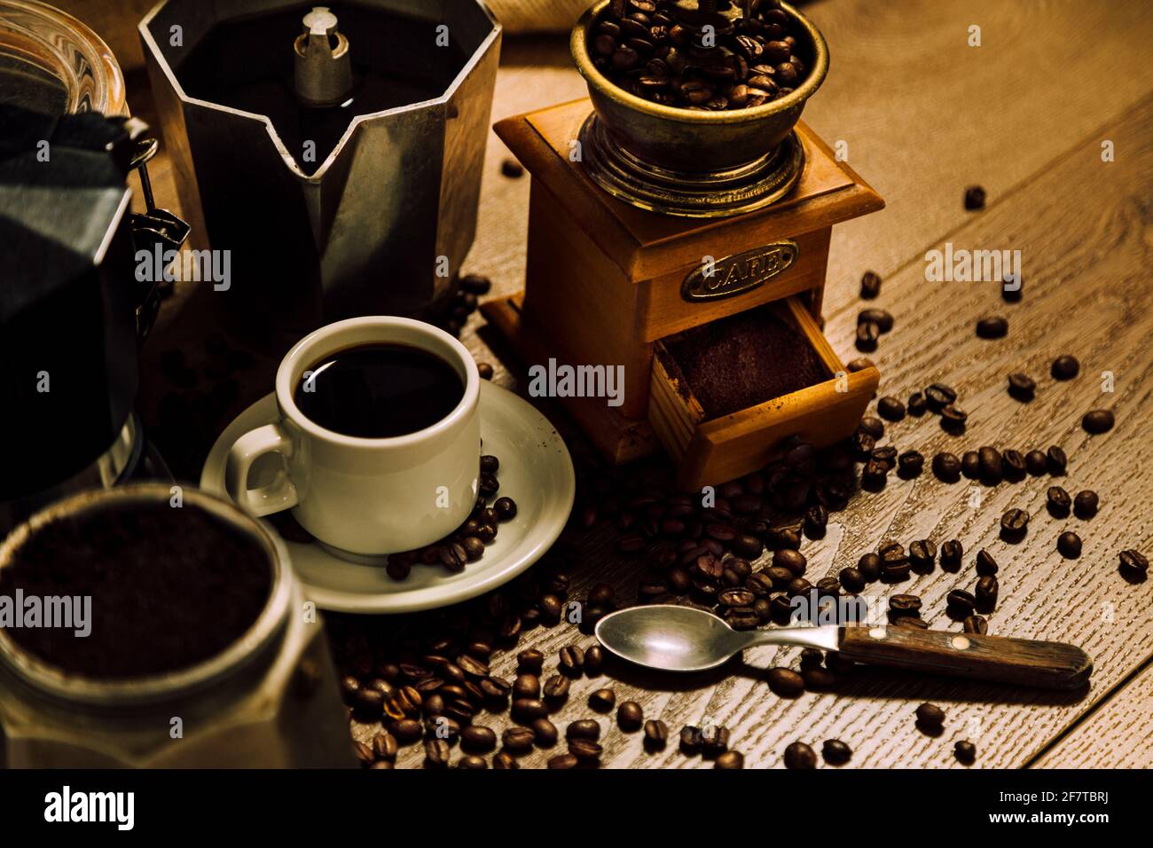 Coffee stuff. A white cup with black coffee, Italian coffee maker moka, a mill and grains over a wooden table. Vintage rustic style. Stock Photo