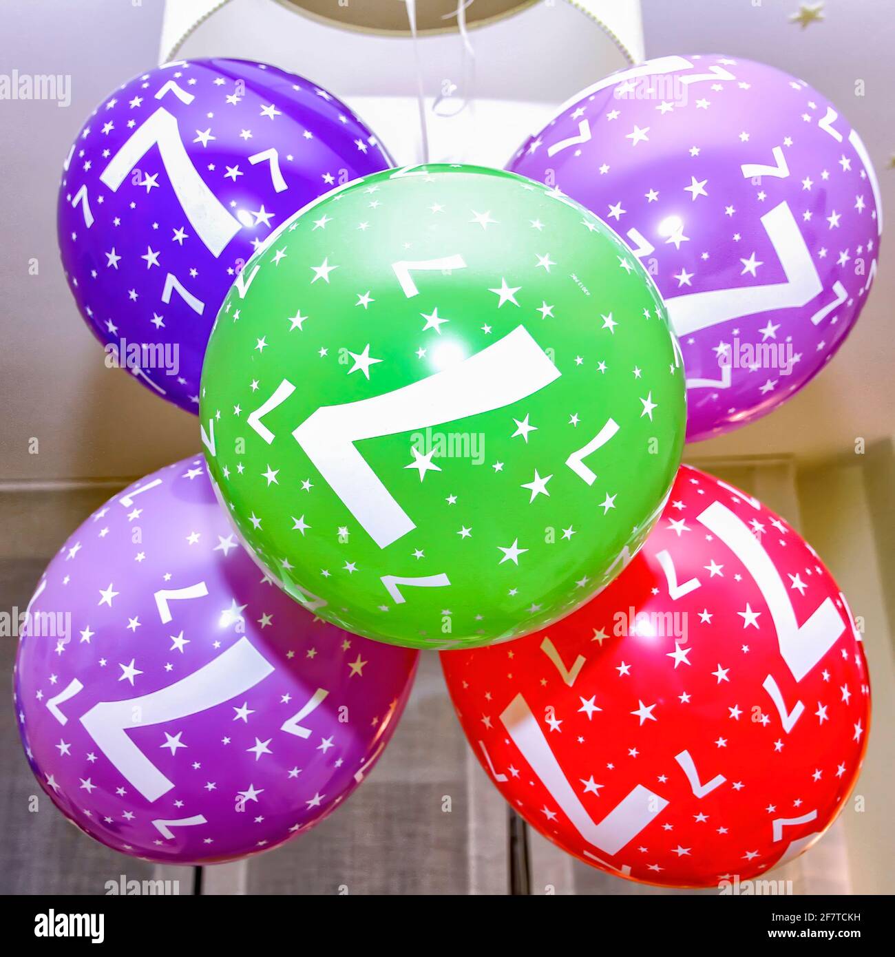 balloons hanging from the lamp of a room with the number 7, birthday balloons of different colors and stars, square format Stock Photo