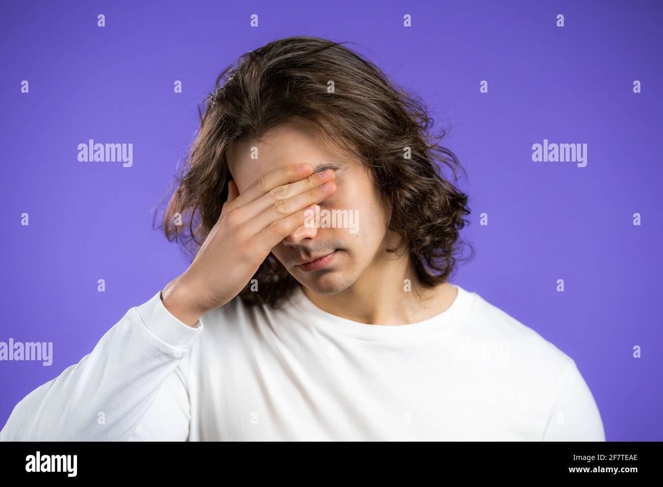 Portrait of young man with long hairstyle doing facepalm gesture, like no, I forgot. Unhappy guy feeling sorrow, regret, drama, failure. He isolated Stock Photo