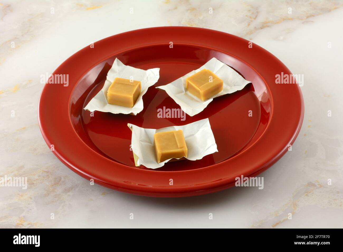 Three creamy caramel candy squares in open candy wrappers on red snack