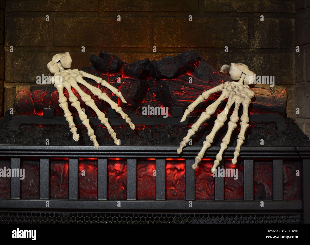 Two skeleton hands grasping onto burning logs in fireplace Stock Photo