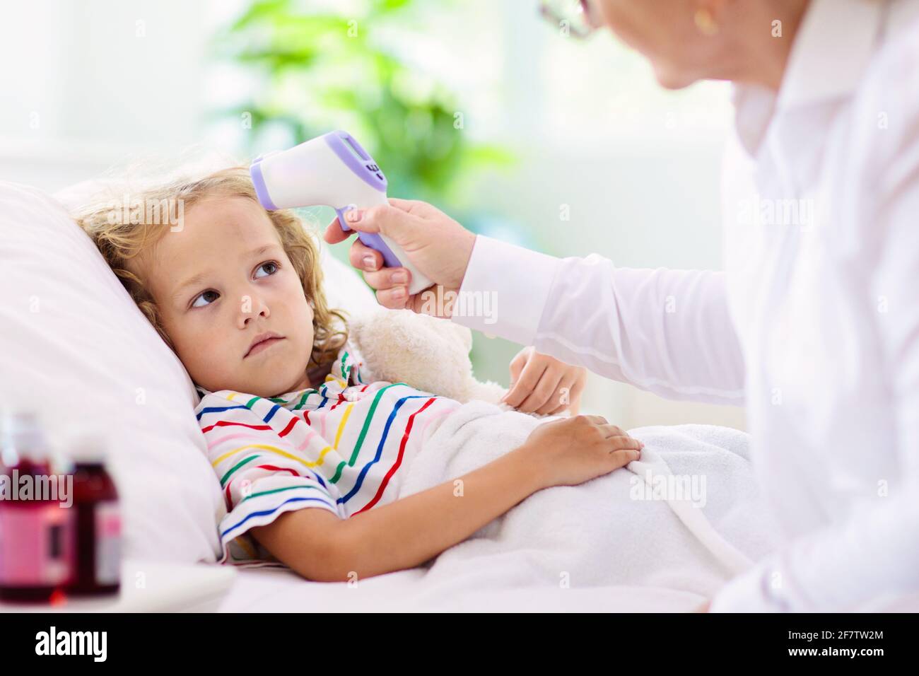 Sick little boy with medicine. Mother checking fever of ill child in bed. Unwell kid with chamber inhaler for asthma cough treatment. Flu season. Stock Photo