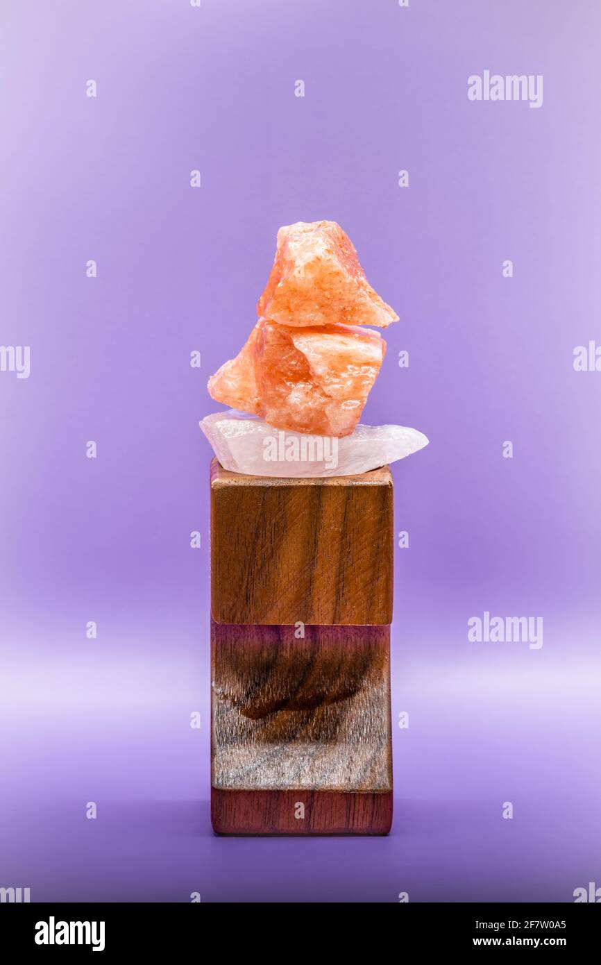 Large chunks of Himalayan sea salt are stacked on top of each other for peace and balance. Supported by a wooden stand and isolated against a purple b Stock Photo