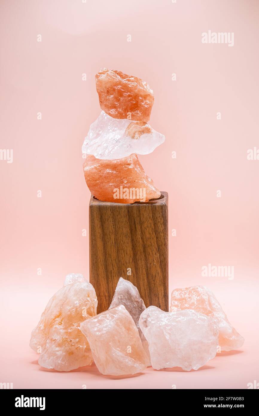 Large chunks of Himalayan sea salt are stacked on top of each other for peace and balance. Supported by a wooden stand and isolated against a soft pin Stock Photo