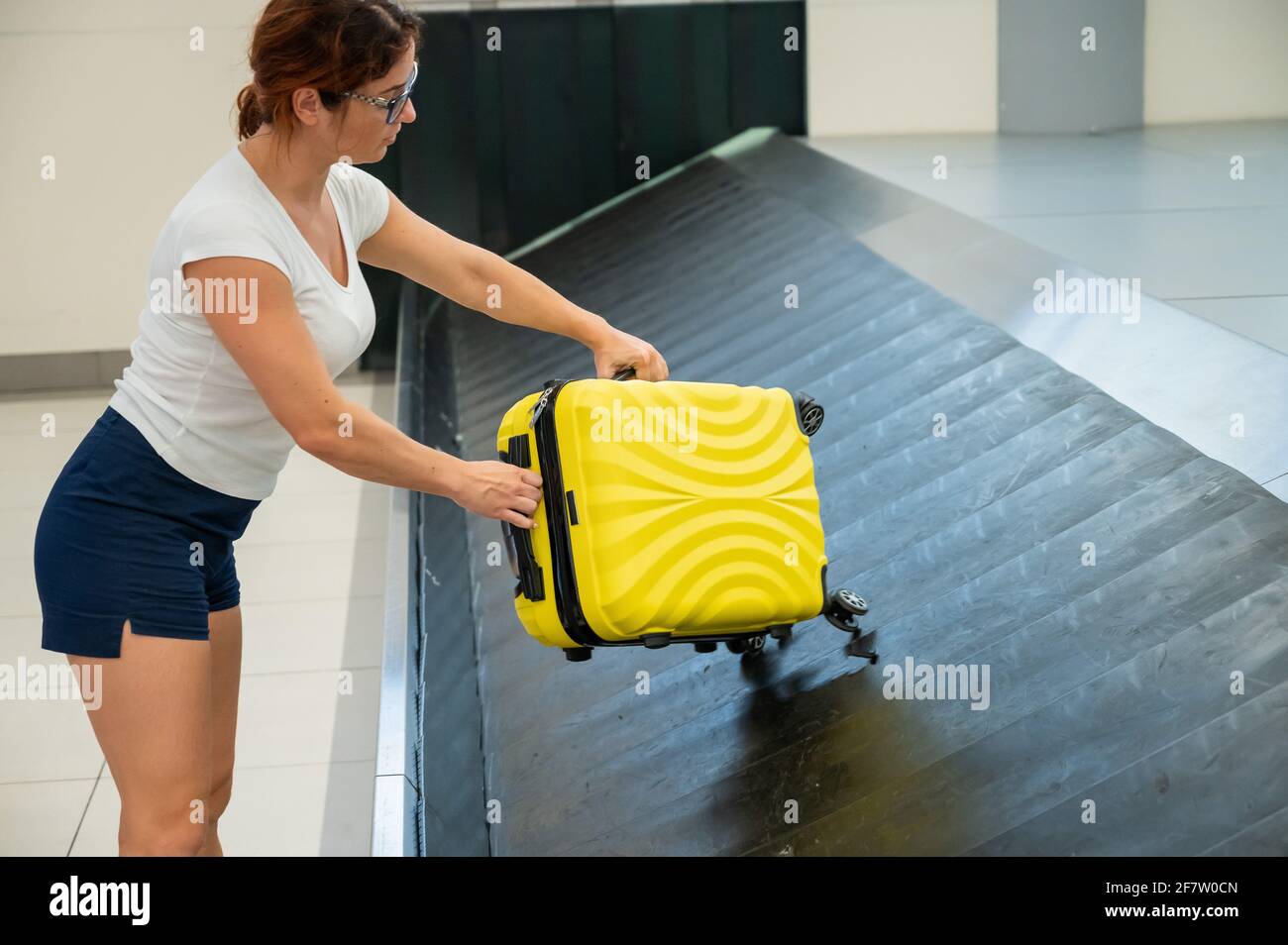 Caucasian woman picks up her yellow suitcase from the luggage belt at