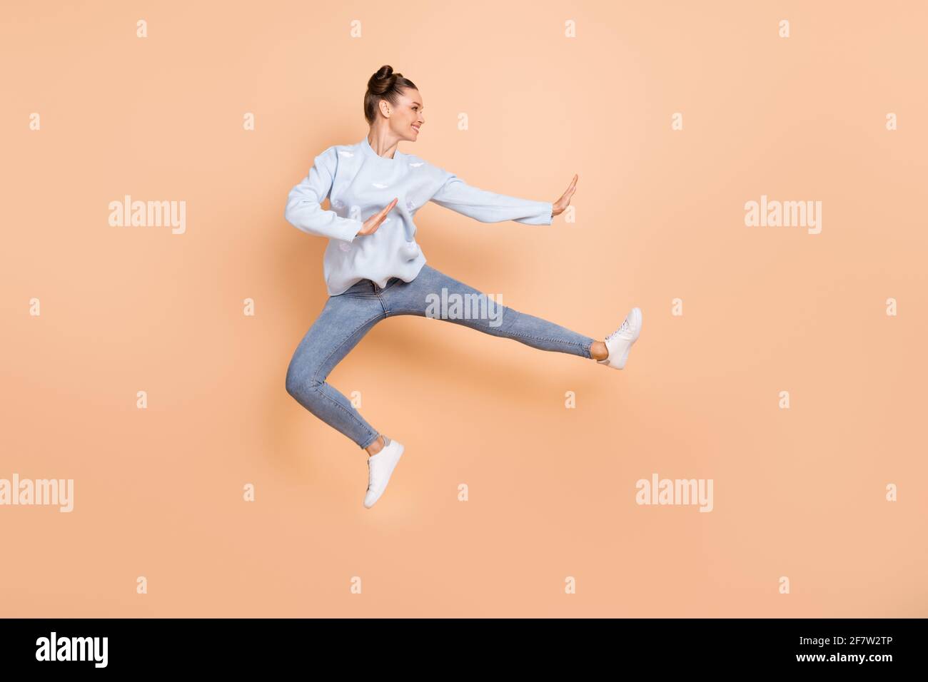 Full size profile photo of optimistic nice brunette lady jump karate wear  blue sweater jeans sneakers isolated on beige background Stock Photo - Alamy