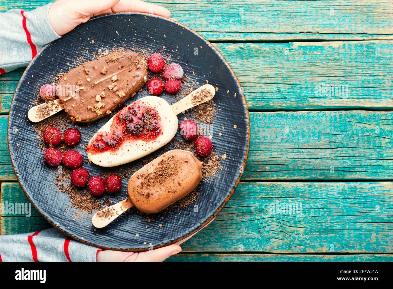 Chocolate covered ice cream with cherry jam on wooden table.Hand holding ice cream Stock Photo