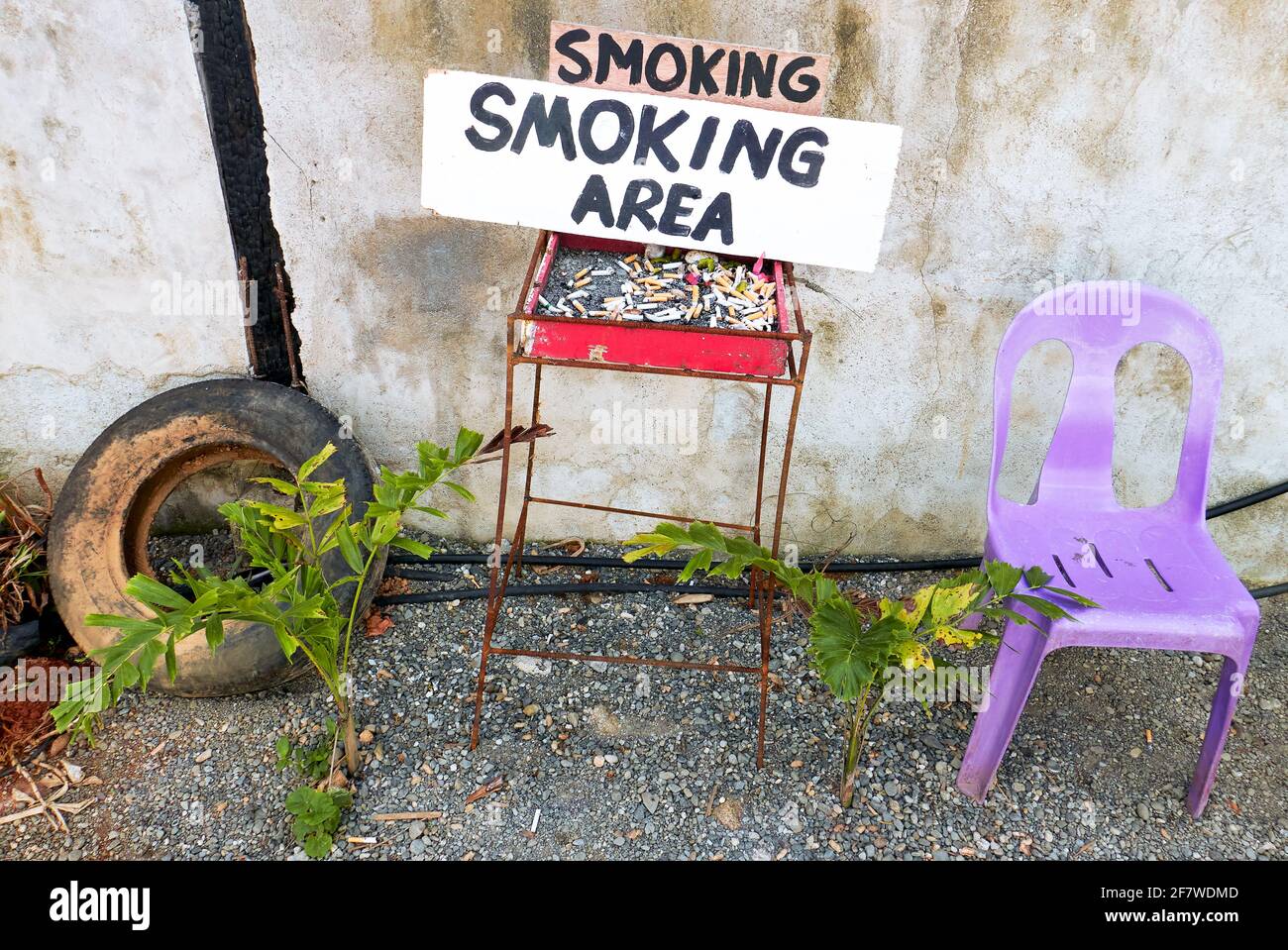 Improvised smoking area wit an ash tray full of cigarette butts placed outside next to a dirty wall, with one plastic chair for the smoker, Asia Stock Photo