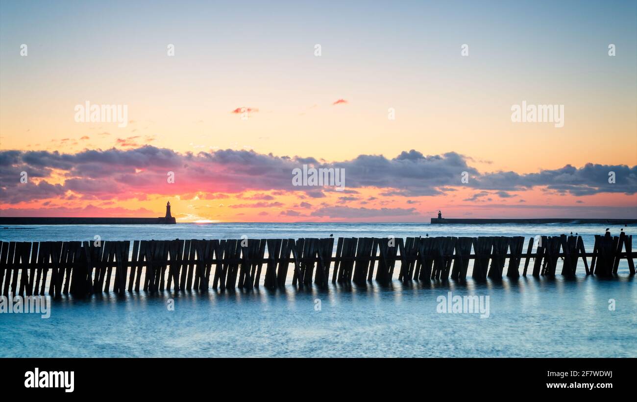 Sunrise at the mouth of the River Tyne captured from the Fish Quay Beach near to Tynemouth Lifeboat Station in North Shields. Old groynes stand in the Stock Photo