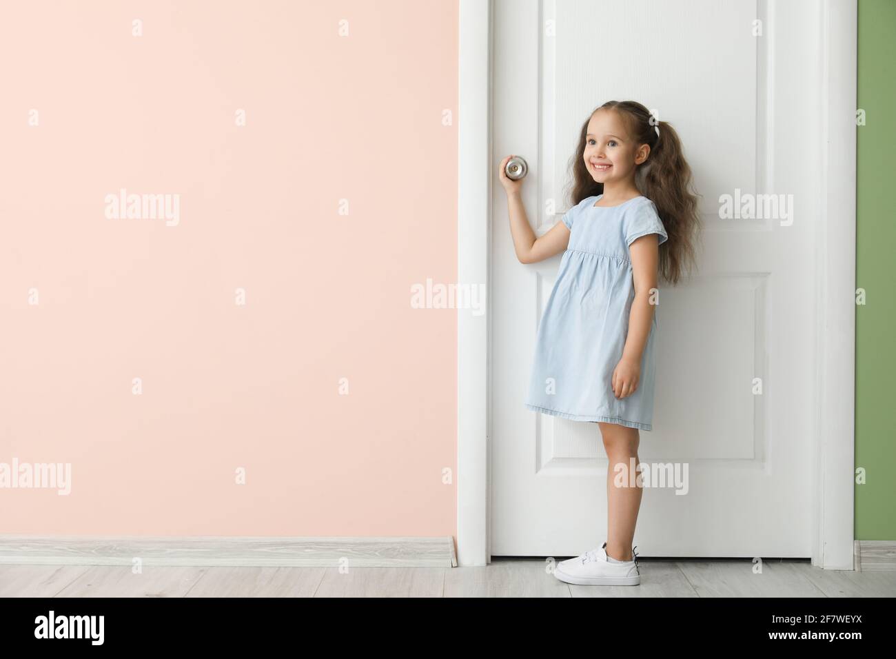 Cute little girl standing near closed door Stock Photo