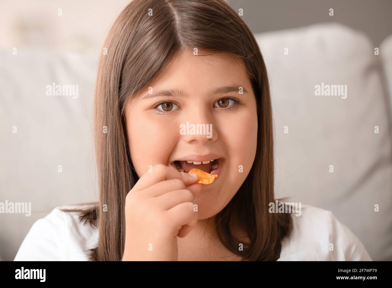 Overweight girl eating unhealthy chips at home Stock Photo