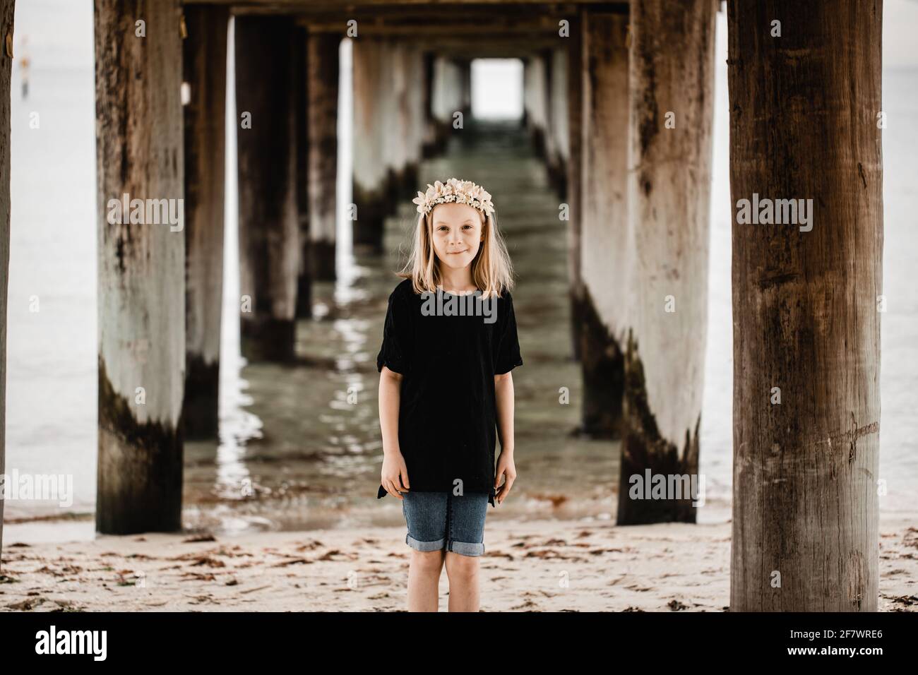 Caucasian girl standing underneath a pier at the beach wearing a flower head band Stock Photo