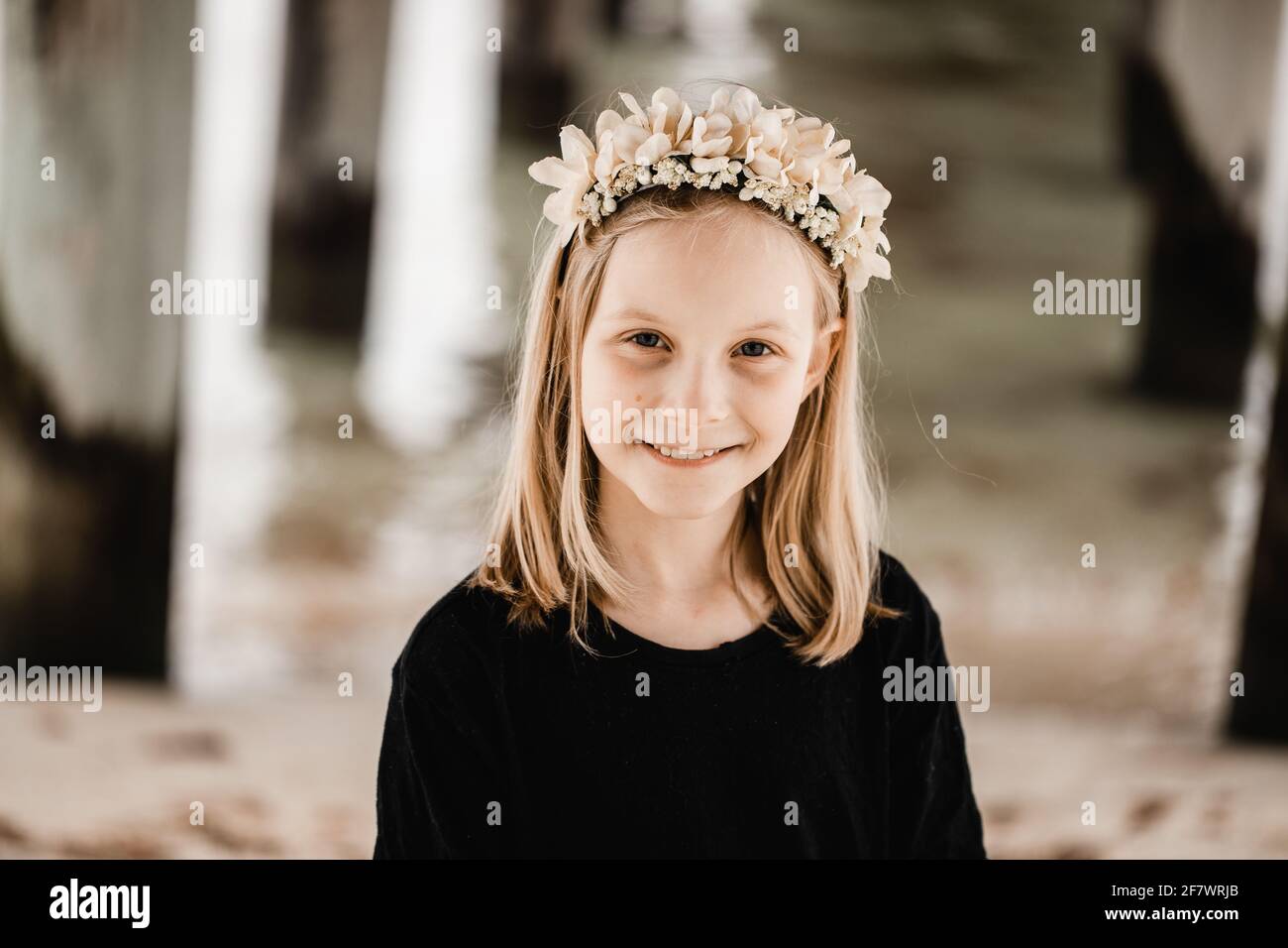 Caucasian girl standing underneath a pier at the beach wearing a flower head band Stock Photo