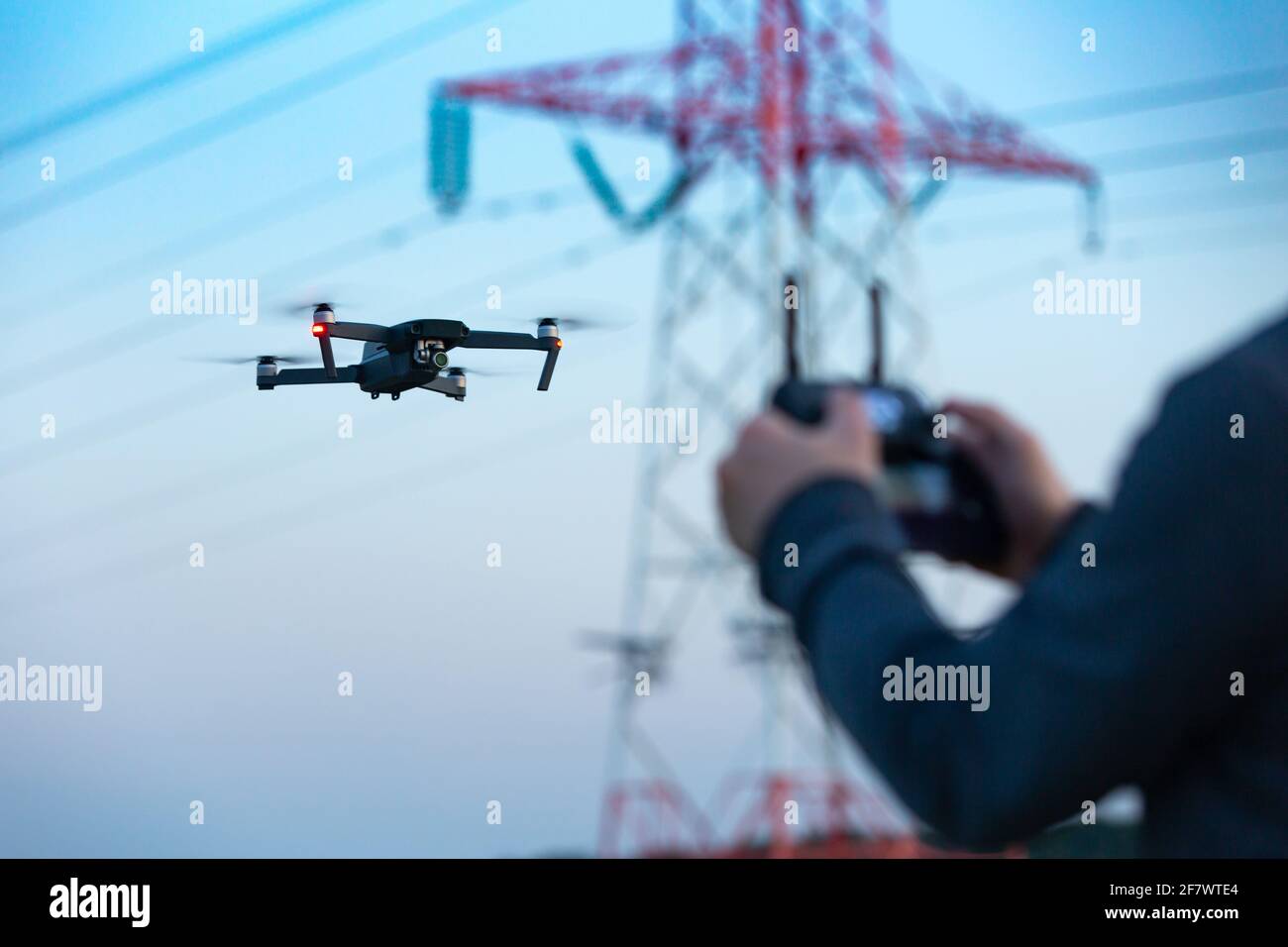 Pilot flying a drone collecting the data remotely from a power tower station or for telecommunication. Drone safety, power transmission tower. Stock Photo