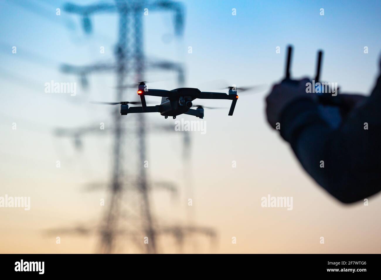 Pilot flying a drone collecting the data remotely from a power tower station or for telecommunication. Drone safety, power transmission tower. Stock Photo