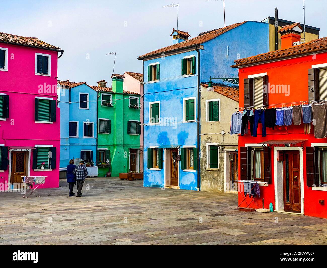 Old peoples walking in the typical and very colorful streets of Burano. We see laundry being dried outside Stock Photo