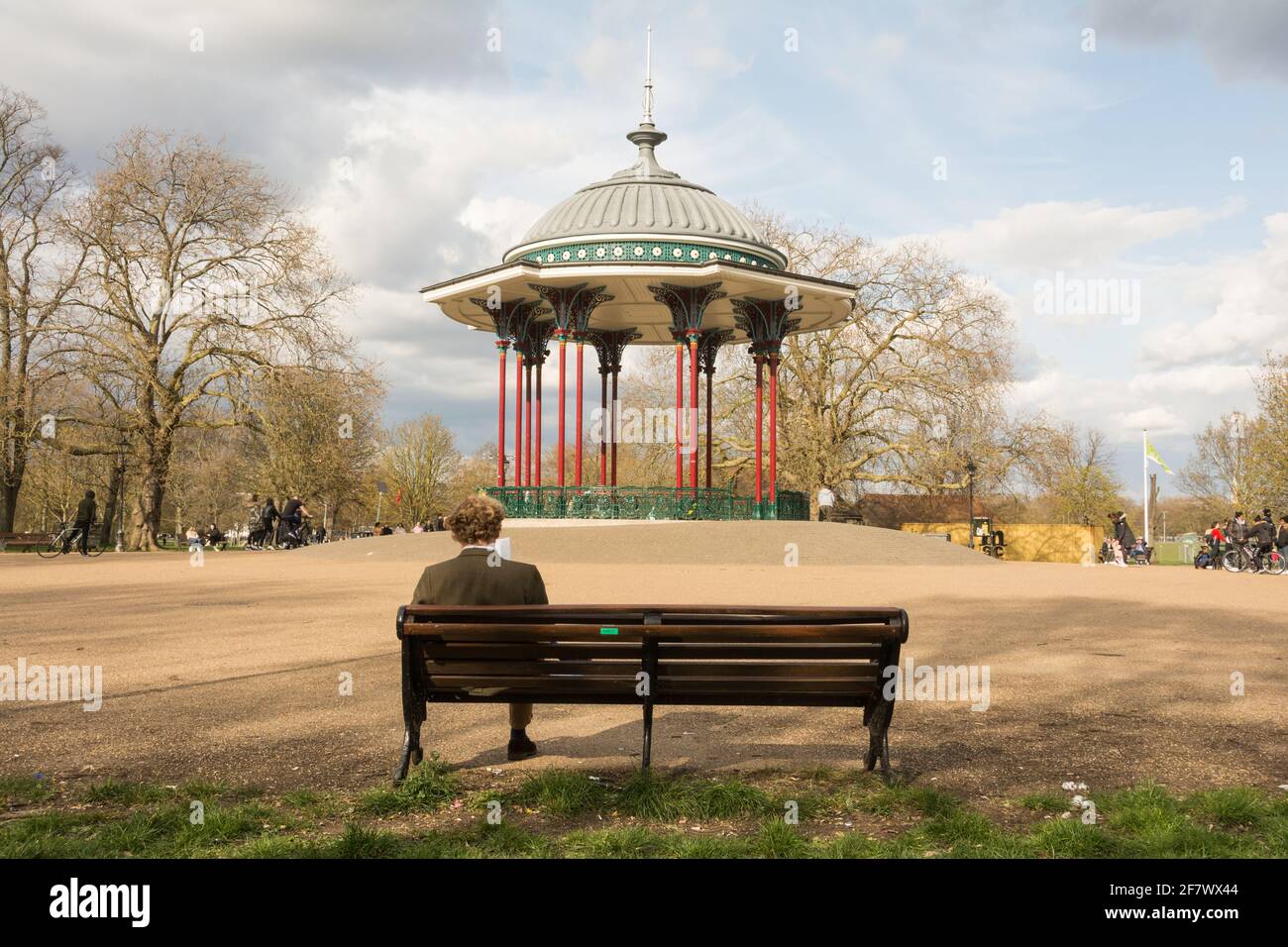 A middle-aged man sitting on a park bench near Clapham Common Bandstand, Windmill Drive, Clapham Common, Clapham, SW4, London, England, U.K. Stock Photo