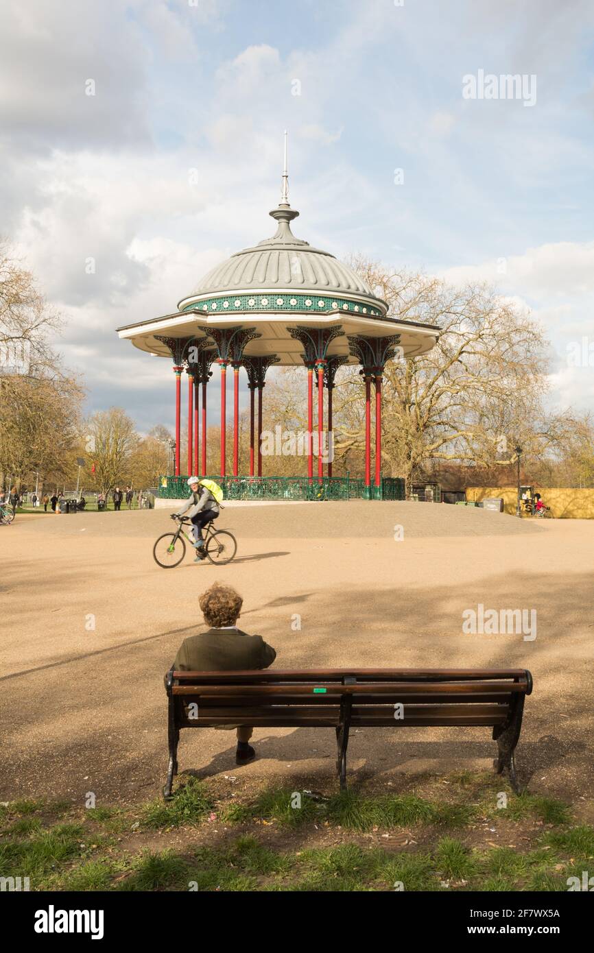 A man sitting on a park bench next to Clapham Common Bandstand, Windmill Drive, Clapham Common, Clapham, SW4, London, England, U.K. Stock Photo
