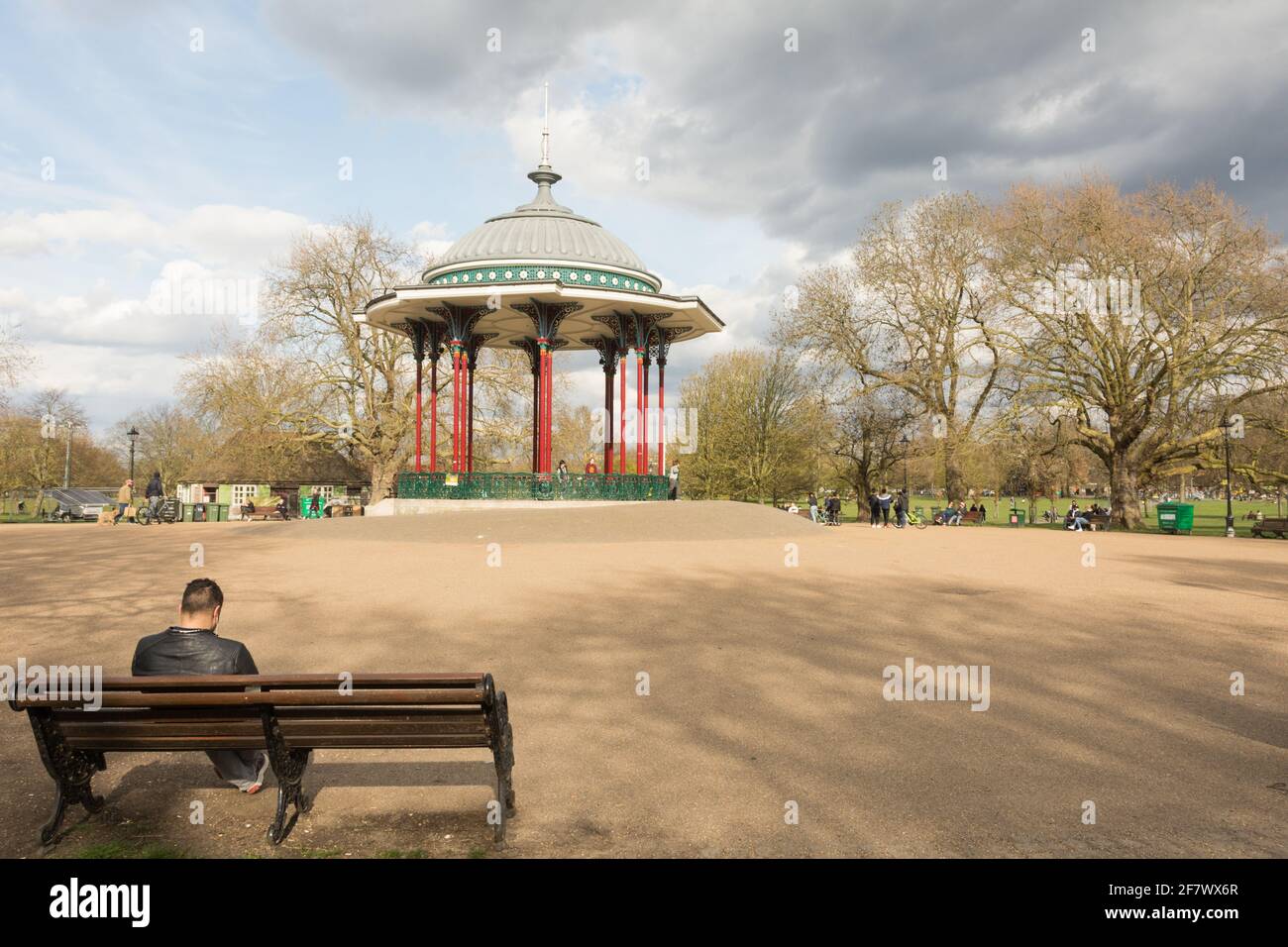 A young man sitting on a park bench next to Clapham Common Bandstand, Windmill Drive, Clapham Common, Clapham, SW4, London, England, U.K. Stock Photo