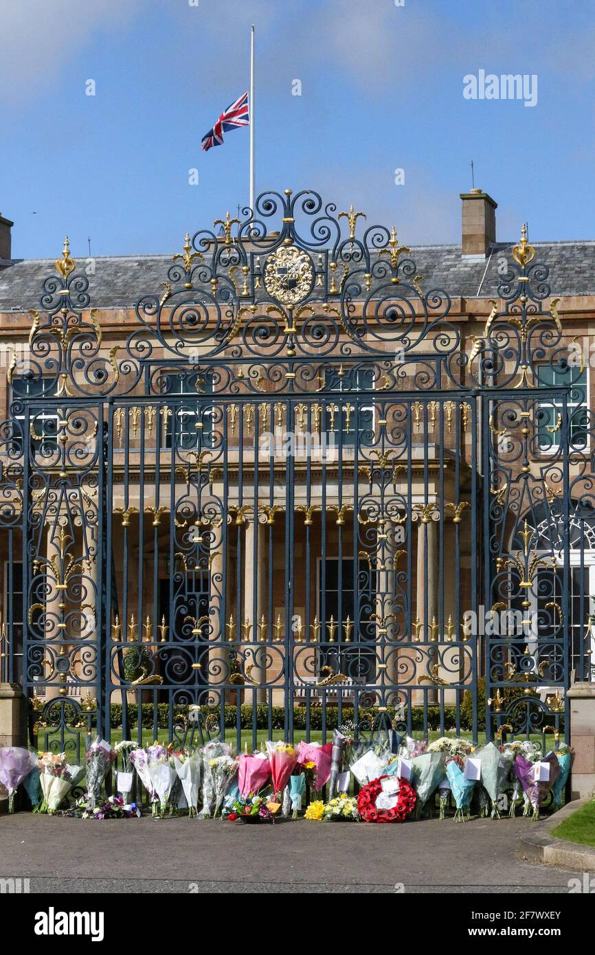 Hillsborough Castle, Hillsborough, County Down, Northern Ireland, UK. 10 April 2021. With the Union flag at half-mast, floral tributes have been left outside the gates of HM The Queen's official residence in Northern Ireland as the public mourn the loss of Prince Philip, Duke of Edinburgh, who died yesterday. Credit: David Hunter/Alamy Live News. Stock Photo