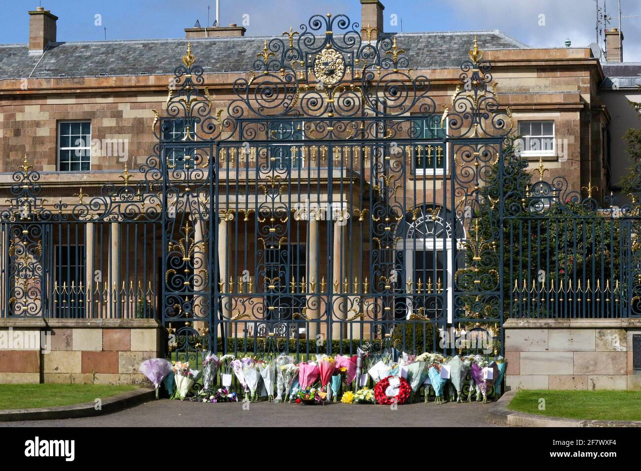 Hillsborough Castle, Hillsborough, County Down, Northern Ireland, UK. 10 April 2021. With the Union flag at half-mast, floral tributes have been left outside the gates of HM The Queen's official residence in Northern Ireland as the public mourn the loss of Prince Philip, Duke of Edinburgh, who died yesterday. Credit: David Hunter/Alamy Live News. Stock Photo