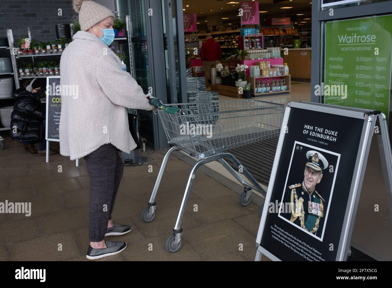 Glasgow, UK, 10th April 2021. Shoppers, wearing facemasks due to the Covid-19 CoronaVirus health pandemic, pass by a tribute to His Royal Highness Prince Philip, Duke of Edinburgh, displayed outside a Waitrose supermarket, as the nation mourns his death at the age of 99-years. Photo credit: Jeremy Sutton-Hibbert/Alamy Live News Stock Photo