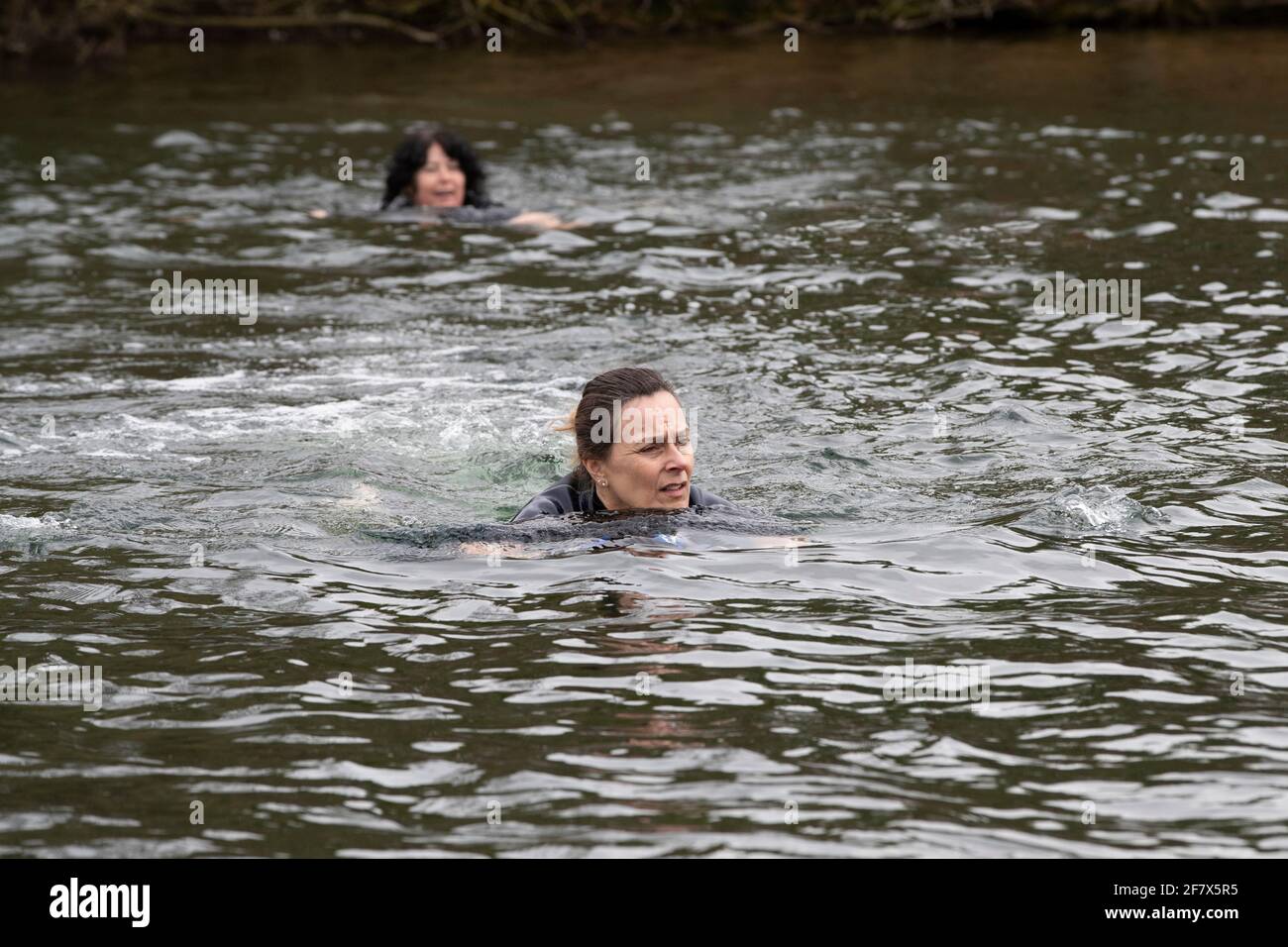 Northampton, UK. 10th April 2021. Shirley Payne Mann with support from  Denise Anderson and Penny Etheridge (left to right) are wild swimming in  freezing water of a lake for as long as