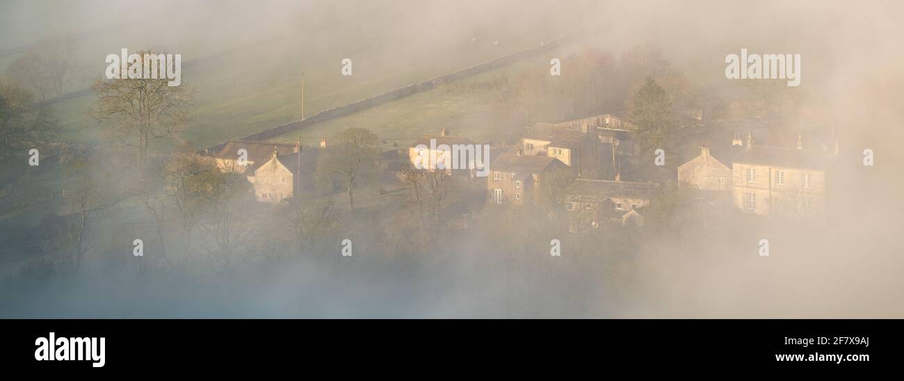 Morning light burns off the mist and reveals the village of Malham in The Yorkshire Dales National Park during a spring temperature inversion. Stock Photo