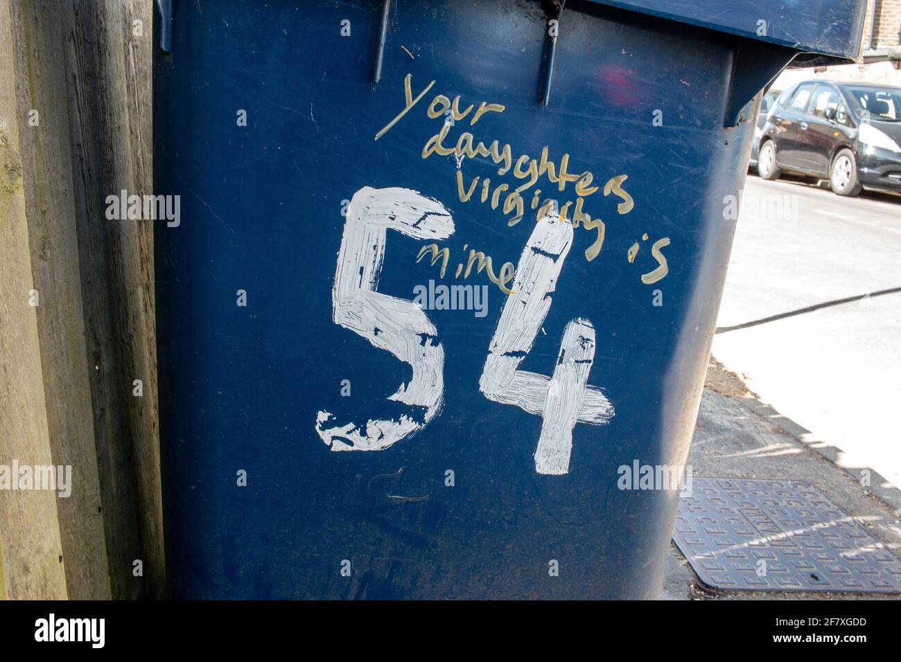 Your Daughter's Virginity Is Mime  -  Misspelled graffiti on a blue wheely bin belonging to house number 54.  Romsey, Cambridge, UK. Stock Photo