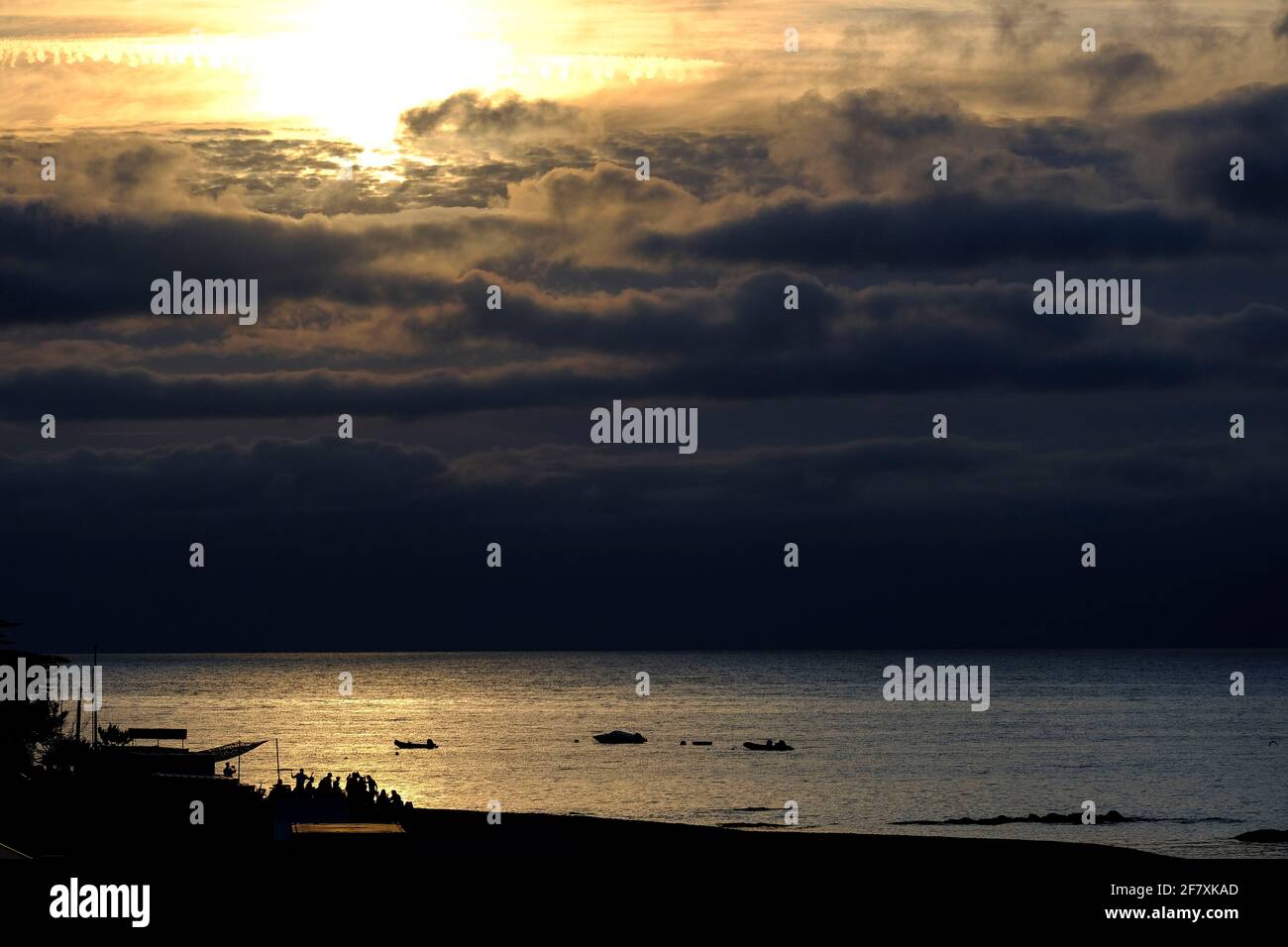 Frankreich, Le Croisic, 19.07.2019: Dramatischer Sonnenuntergang hinter dunklen Wolken hinter einer Strandbar mit Gaesten am Strand von Le Croisic an Stock Photo