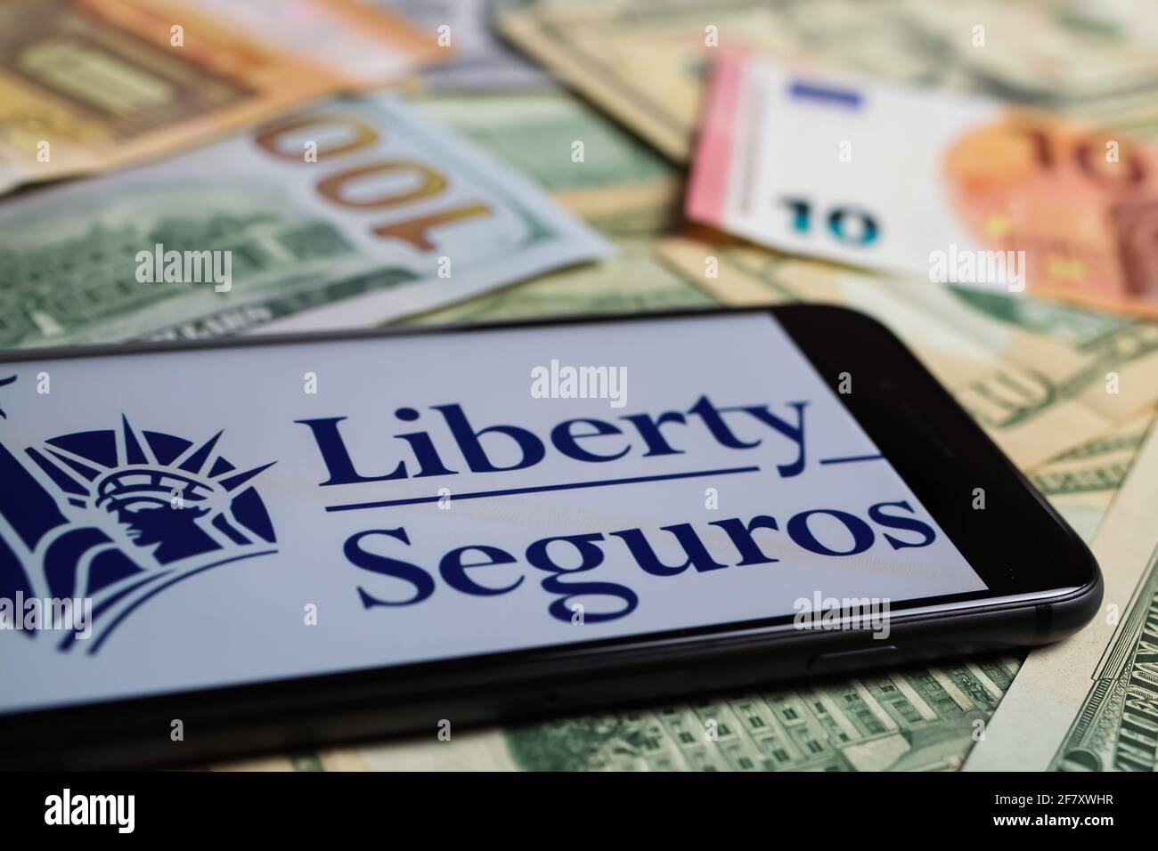 Viersen, Germany - March 1. 2021: Closeup of smartphone with logo lettering of liberty seguros insurance company on paper money currency Stock Photo