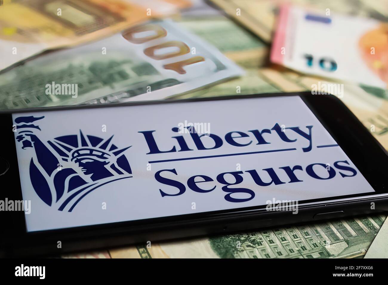 Viersen, Germany - March 1. 2021: Closeup of smartphone with logo lettering of liberty seguros insurance company on paper money currency Stock Photo