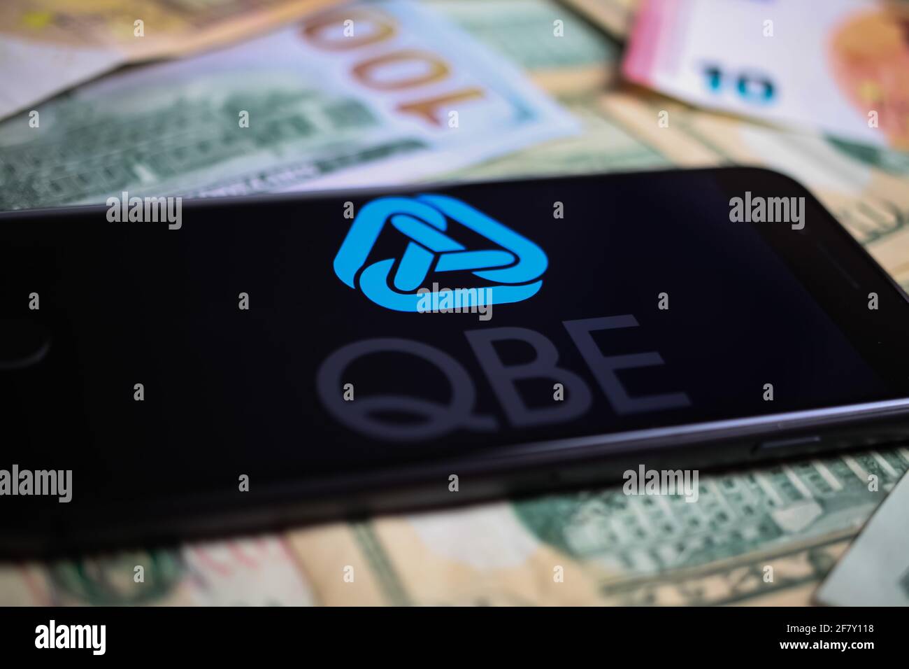 Viersen, Germany - March 1. 2021: Closeup of smartphone with logo lettering of australian qbe insurance company on paper money currency Stock Photo